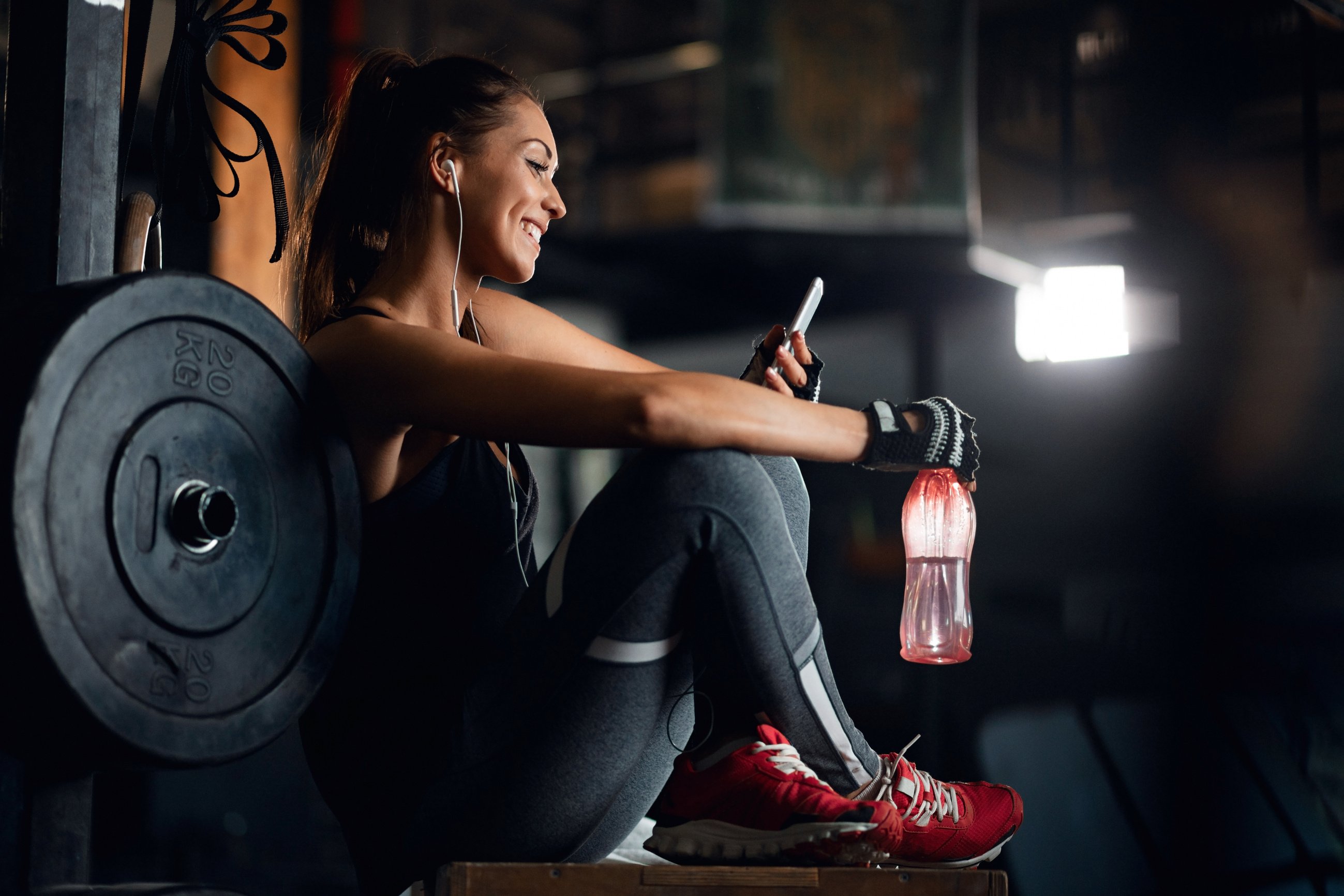 Happy sportswoman using cell phone on water break in a gym.