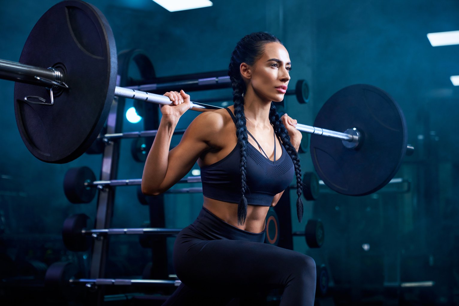 Woman doing bulgarian squats using barbell in gym.